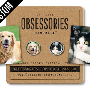 May include: A set of two custom pet portrait pinback buttons. The buttons are made of hypoallergenic surgical steel and feature a golden retriever and a black and white cat. The buttons are displayed on a brown card with the text "OBSESSORIES HANDMADE" and "ACCESSORIES FOR THE OBSESSED".