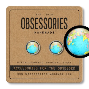 Puede incluir: Un par de pendientes de acero quirúrgico hipoalergénico con un globo terráqueo en miniatura con un diseño de mapa azul y amarillo. Los pendientes se muestran en una tarjeta marrón con el texto "OBSESSORIES HANDMADE" y "ACCESSORIES FOR THE OBSESSED".