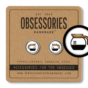 May include: A pair of silver earrings with a white background and a black and orange coffee pot design. The earrings are hypoallergenic and made of surgical steel. The text "OBSESSORIES HANDMADE" is on the card.