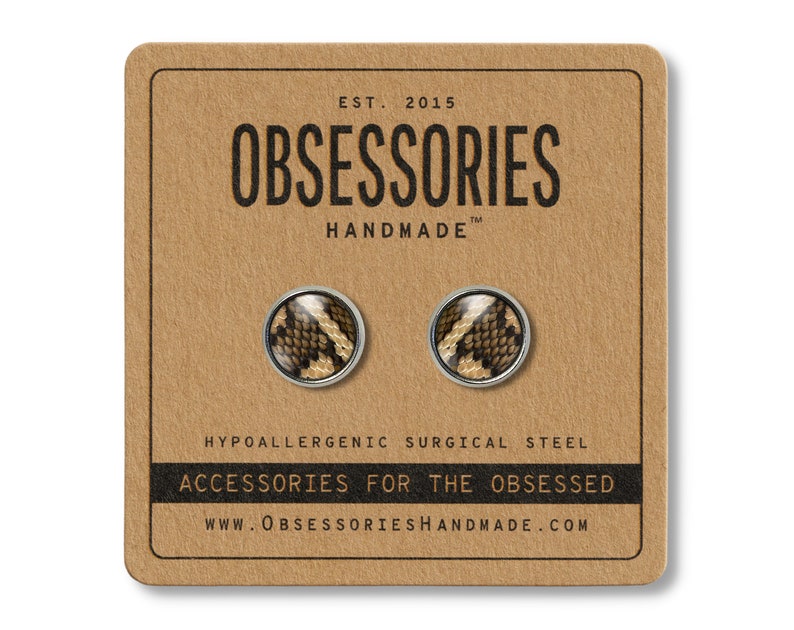 Peut inclure: Boucles d'oreilles &agrave; clous avec un motif peau de serpent, pr&eacute;sent&eacute;es sur une carte marron. Les boucles d'oreilles sont rondes avec un bord en m&eacute;tal argent&eacute;. La carte porte le texte "OBSESSORIES HANDMADE" et "ACCESSORIES FOR THE OBSESSED".