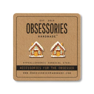 May include: A pair of gingerbread house earrings on a brown card. The earrings are white, orange, and green. The card has the text "OBSESSORIES HANDMADE" and "ACCESSORIES FOR THE OBSESSED".