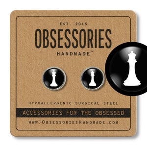 Puede incluir: Un par de gemelos de plata con fondos negros y siluetas blancas de reinas de ajedrez. Los gemelos se muestran en una tarjeta marrón con el texto "OBSESSORIES HANDMADE" y "ACCESSORIES FOR THE OBSESSED".