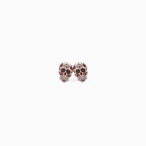 May include: A pair of skull-shaped stud earrings. The earrings feature a detailed design with a white base, adorned with purple, red, and black accents. The skull's eyes and other features are highlighted with small, colorful embellishments.