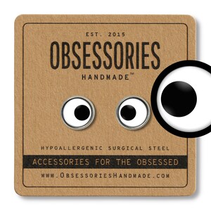May include: A pair of small, white, round earrings with black centers. The earrings are on a brown card with the text "OBSESSORIES HANDMADE" and "ACCESSORIES FOR THE OBSESSED".