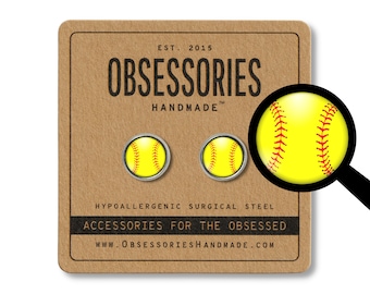 Peut inclure: Une paire de boucles d'oreilles en acier chirurgical hypoallergénique représentant une balle de softball jaune avec des coutures rouges. Les boucles d'oreilles sont présentées sur une carte brune avec le texte "OBSESSORIES HANDMADE" et "ACCESSORIES FOR THE OBSESSED".