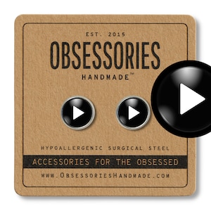 May include: A pair of black play button earrings on a brown background. The earrings are made of hypoallergenic surgical steel. The text "OBSESSORIES HANDMADE" is printed on the background. The text "ACCESSORIES FOR THE OBSESSED" is printed below the logo. The website address "WWW.OBSESSORIESHANDMADE.COM" is printed below the text.