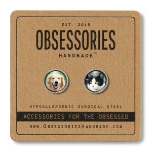 May include: A pair of hypoallergenic surgical steel earrings featuring a golden retriever and a black and white cat. The earrings are on a brown card with the text "OBSESSORIES HANDMADE" and "ACCESSORIES FOR THE OBSESSED".