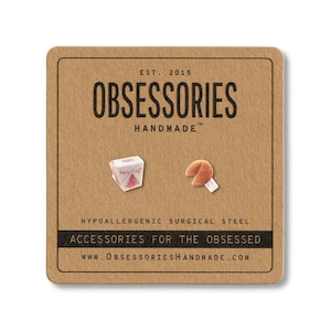 May include: A pair of stud earrings on a brown card. One earring is a miniature Chinese takeout box, the other is a fortune cookie. The card reads "OBSESSORIES HANDMADE" and "ACCESSORIES FOR THE OBSESSED."