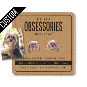 May include: Custom dog-themed stud earrings on a brown card. The card features the text "OBSESSORIES HANDMADE" and "ACCESSORIES FOR THE OBSESSED". A photo of a dog is on the card, with two matching dog face earrings.