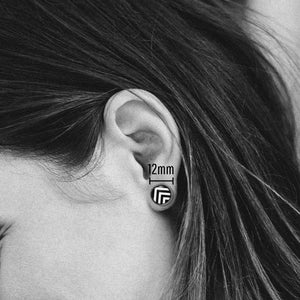 May include: A black and white geometric pattern earring with a 12mm diameter. The earring is worn in a person's ear.