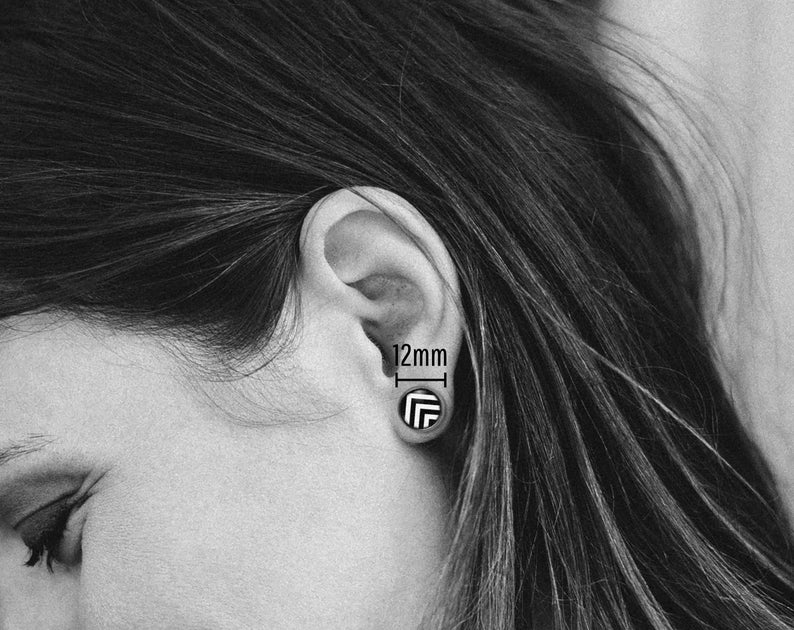 May include: A black and white geometric pattern earring with a 12mm diameter. The earring is worn in a person's ear.
