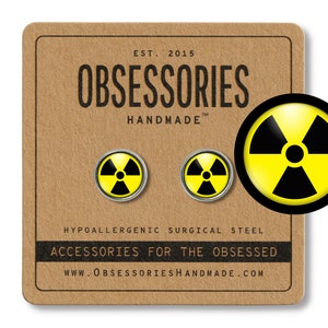 May include: A pair of round stud earrings featuring a yellow and black radiation symbol. The earrings are on a brown card with the text "OBSESSORIES HANDMADE" and "ACCESSORIES FOR THE OBSESSED".