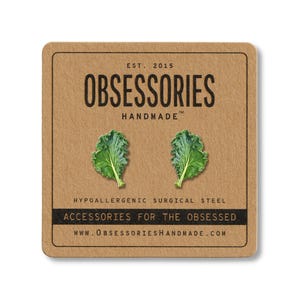 May include: A square, tan product tag with the text "OBSESSORIES HANDMADE" and two green kale leaf earrings. The tag also includes the text "ACCESSORIES FOR THE OBSESSED" and "HYPOALLERGENIC SURGICAL STEEL".
