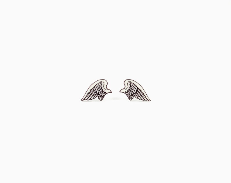 Puede incluir: Un par de pendientes peque&ntilde;os con forma de alas, blancos y negros. Cada ala tiene un dise&ntilde;o detallado de plumas. Los pendientes son sim&eacute;tricos y se presentan sobre un fondo blanco liso, resaltando su delicado dise&ntilde;o.