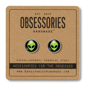 May include: A pair of green alien face stud earrings on a brown card with the text "OBSESSORIES HANDMADE" and "ACCESSORIES FOR THE OBSESSED".