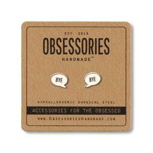 May include: A pair of silver-colored stud earrings shaped like speech bubbles, each with the word "BYE" in black. The earrings are displayed on a brown card with the text "OBSESSORIES HANDMADE" and "ACCESSORIES FOR THE OBSESSED".