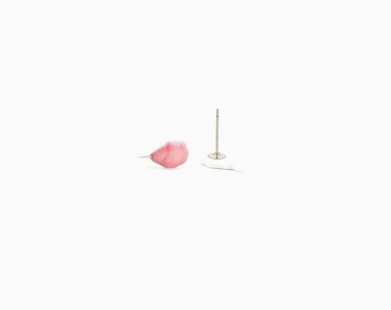 May include: A single pink petal and a silver earring post with a white backing are set against a white background. The petal has a delicate, translucent appearance with a gradient of pink hues.
