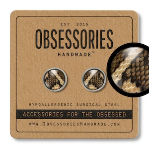 Op de afbeelding: Ronde oorstekers met een slangenprint, gepresenteerd op een bruine kaart. De kaart toont de tekst "OBSESSORIES HANDMADE" en "ACCESSORIES FOR THE OBSESSED". De oorbellen zijn gemaakt van hypoallergeen chirurgisch staal.