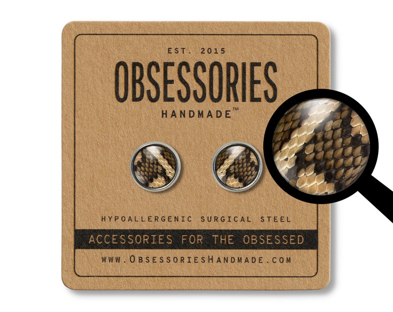 Peut inclure: Boucles d'oreilles &agrave; clous rondes avec un motif peau de serpent, pr&eacute;sent&eacute;es sur une carte marron. La carte indique "OBSESSORIES HANDMADE" et "ACCESSORIES FOR THE OBSESSED". Les boucles sont en acier chirurgical hypoallerg&eacute;nique.