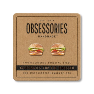 May include: A square, brown card with the text "OBSESSORIES HANDMADE" and two miniature hamburger earrings. The card also includes the text "ACCESSORIES FOR THE OBSESSED" and "WWW.OBSESSORIESHANDMADE.COM".
