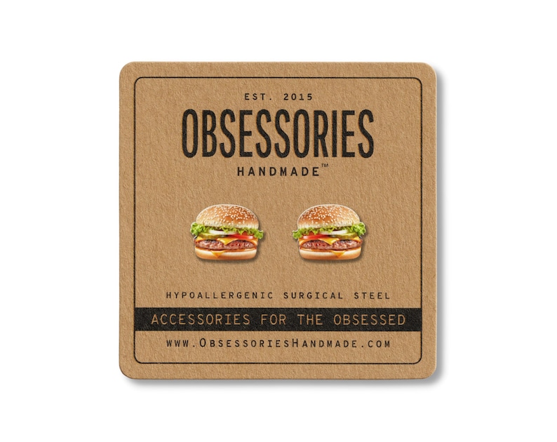 May include: A square, brown card with the text "OBSESSORIES HANDMADE" and two miniature hamburger earrings. The card also includes the text "ACCESSORIES FOR THE OBSESSED" and "WWW.OBSESSORIESHANDMADE.COM".