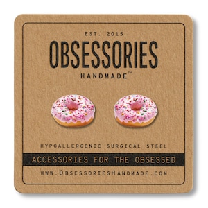 Puede incluir: Una tarjeta marrón con el texto "EST. 2015 OBSESSORIES HANDMADE TM" y el texto "HYPOALLERGENIC SURGICAL STEEL ACCESSORIES FOR THE OBSESSED WWW.OBSESSORIESHANDMADE.COM". Se muestran dos donuts rosados glaseados con chispas de colores en la tarjeta.
