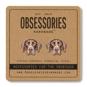 Può includere: Un paio di orecchini a bottone con un cane Bracco tedesco a pelo corto marrone e bianco su una carta marrone con il testo "OBSESSORIES HANDMADE" e "ACCESSORIES FOR THE OBSESSED".