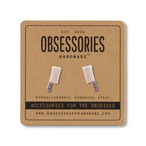 May include: A pair of novelty cleaver earrings on a brown card. The earrings are white with a silver handle and blue dots. The card reads "OBSESSORIES HANDMADE" and "ACCESSORIES FOR THE OBSESSED."