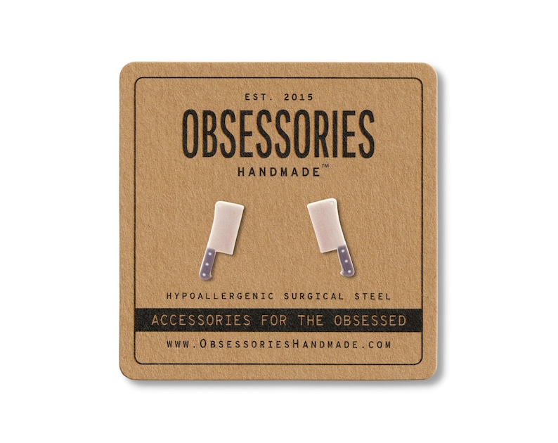 May include: A pair of novelty cleaver earrings on a brown card. The earrings are white with a silver handle and blue dots. The card reads "OBSESSORIES HANDMADE" and "ACCESSORIES FOR THE OBSESSED."