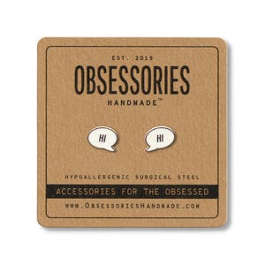 May include: A pair of silver-colored "Hi" speech bubble earrings on a brown card. The card has the text "OBSESSORIES HANDMADE" and "ACCESSORIES FOR THE OBSESSED". The earrings are made of hypoallergenic surgical steel.