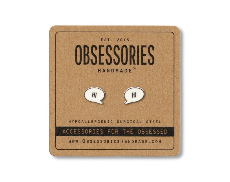 May include: A pair of silver-colored "Hi" speech bubble earrings on a brown card. The card has the text "OBSESSORIES HANDMADE" and "ACCESSORIES FOR THE OBSESSED". The earrings are made of hypoallergenic surgical steel.