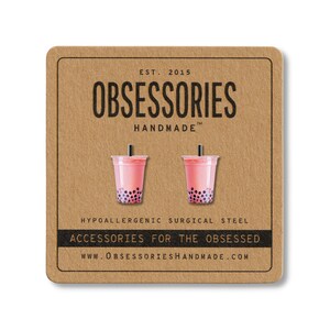 May include: A pair of pink bubble tea earrings with black boba pearls, displayed on a brown card. The card features the text "OBSESSORIES HANDMADE" and "ACCESSORIES FOR THE OBSESSED". The earrings are made of hypoallergenic surgical steel.
