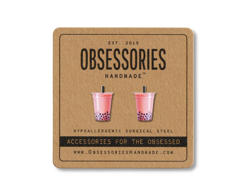 May include: A pair of pink bubble tea earrings with black boba pearls, displayed on a brown card. The card features the text "OBSESSORIES HANDMADE" and "ACCESSORIES FOR THE OBSESSED". The earrings are made of hypoallergenic surgical steel.