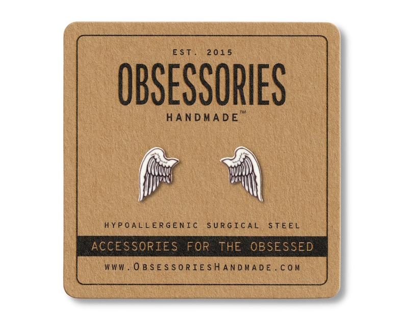 Puede incluir: Pendientes plateados con forma de ala sobre una tarjeta marr&oacute;n. La tarjeta tiene el texto "OBSESSORIES HANDMADE" y "ACCESSORIES FOR THE OBSESSED". Los pendientes son de acero quir&uacute;rgico hipoalerg&eacute;nico.