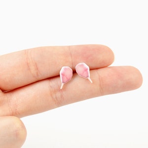 May include: A pair of delicate, pink petal-shaped earrings with white stems. The earrings are small and lightweight, perfect for everyday wear. The earrings are a charming accessory for those who appreciate floral designs.