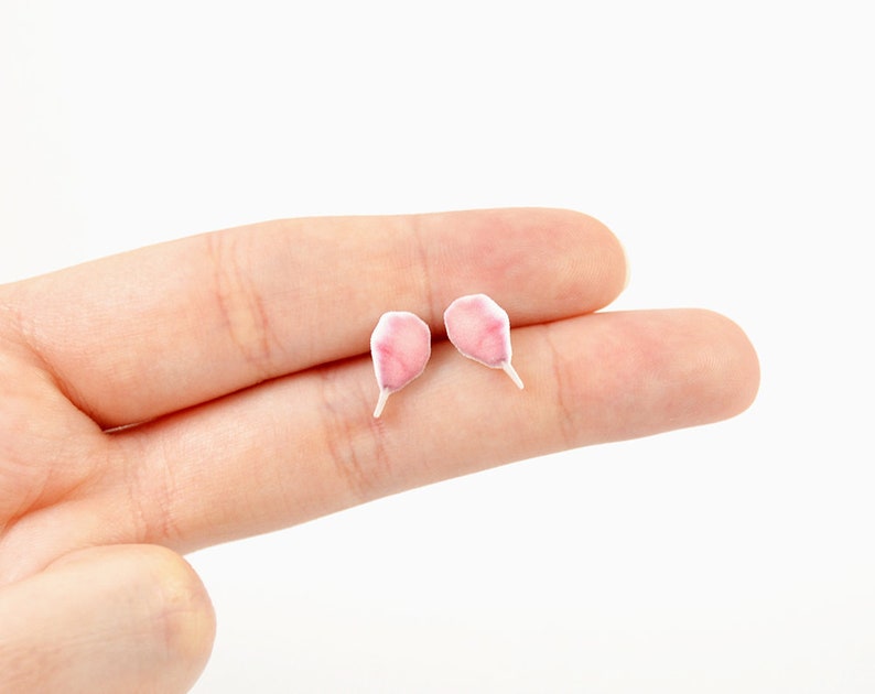 May include: A pair of delicate, pink petal-shaped earrings with white stems. The earrings are small and lightweight, perfect for everyday wear. The earrings are a charming accessory for those who appreciate floral designs.