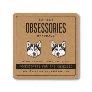 May include: A pair of silver-colored husky dog stud earrings on a brown card. The card reads "OBSESSORIES HANDMADE" and "ACCESSORIES FOR THE OBSESSED". The earrings are made of hypoallergenic surgical steel.