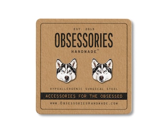 May include: A pair of silver-colored husky dog stud earrings on a brown card. The card reads "OBSESSORIES HANDMADE" and "ACCESSORIES FOR THE OBSESSED". The earrings are made of hypoallergenic surgical steel.