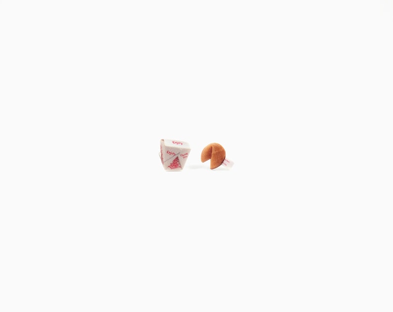 May include: A fortune cookie with a visible fortune and a Chinese takeout box with red text and a tree design. The fortune cookie is brown and open, revealing a white slip of paper. The takeout box is white with red accents.