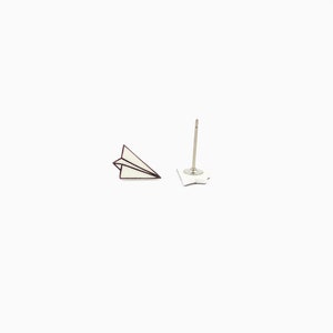 May include: A pair of paper airplane stud earrings. The earrings feature a white paper airplane design with a dark outline. One earring is a complete paper airplane, and the other is the post and backing.