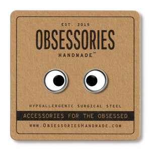 May include: A pair of silver-colored earrings with white and black googly eyes. The earrings are hypoallergenic and made of surgical steel. The card reads "OBSESSORIES HANDMADE" and "ACCESSORIES FOR THE OBSESSED".