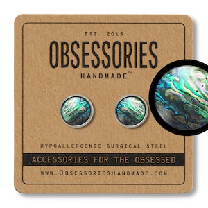 Op de afbeelding: Een paar hypoallergene oorringen van chirurgisch staal met een ontwerp van groene en blauwe abalone-schelp. De oorringen worden gepresenteerd op een bruine kaart met de tekst "OBSESSORIES HANDMADE" en "ACCESSORIES FOR THE OBSESSED".