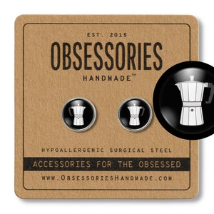 May include: A pair of silver earrings with black enamel and a white silhouette of a coffee pot. The earrings are on a brown background with the text "OBSESSORIES HANDMADE" and "ACCESSORIES FOR THE OBSESSED".