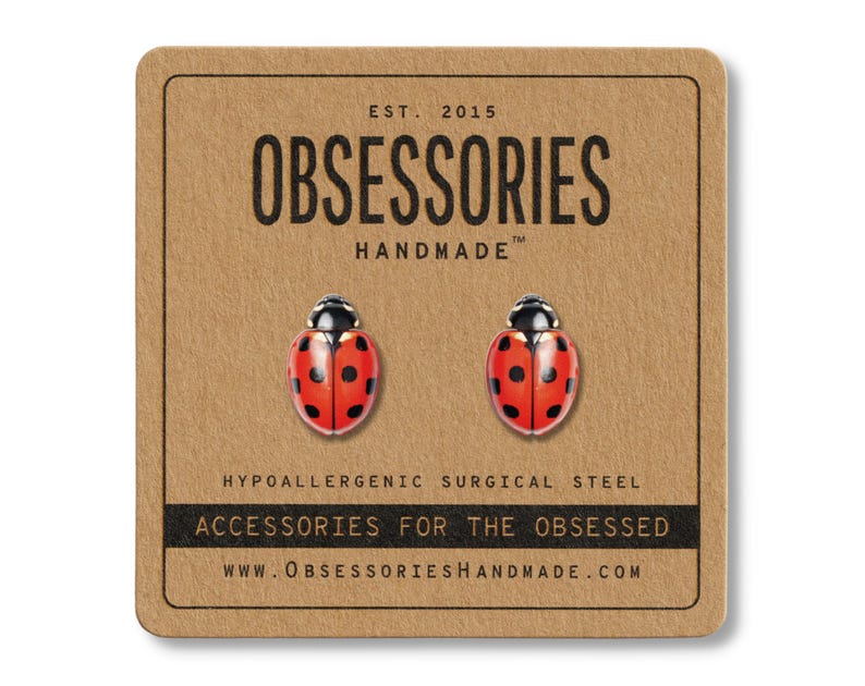 May include: A pair of ladybug stud earrings on a brown card. The earrings are red with black spots and a black head. The card has the text "OBSESSORIES HANDMADE" and "ACCESSORIES FOR THE OBSESSED".