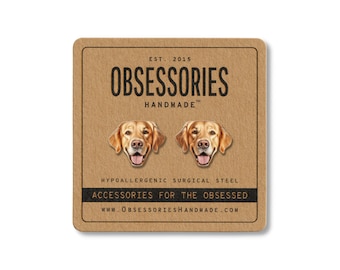 May include: A pair of golden retriever dog face stud earrings on a brown card. The card reads "OBSESSORIES HANDMADE" and "ACCESSORIES FOR THE OBSESSED". The earrings are made of hypoallergenic surgical steel.