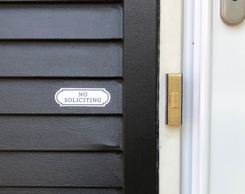 Puede incluir: Una puerta negra con un letrero blanco que dice "NO SOLICITING" y un bot&oacute;n de timbre dorado.