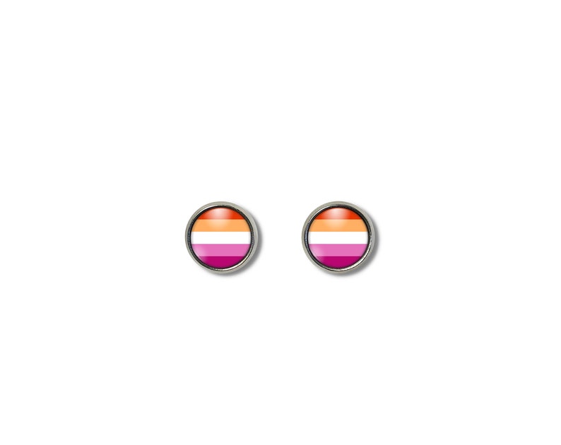 May include: Two round stud earrings with a silver-colored border. Each earring features the lesbian pride flag design, with horizontal stripes of orange, white, and pink. The earrings are set against a white background.