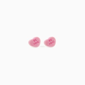 May include: Two pink heart-shaped candies with the words "BE MINE" printed on them. The candies are on a white background. These candies are a classic Valentine's Day treat.