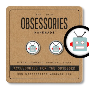 May include: A pair of silver robot earrings with red accents. The earrings are on a brown card with the text "OBSESSORIES HANDMADE" and "ACCESSORIES FOR THE OBSESSED".