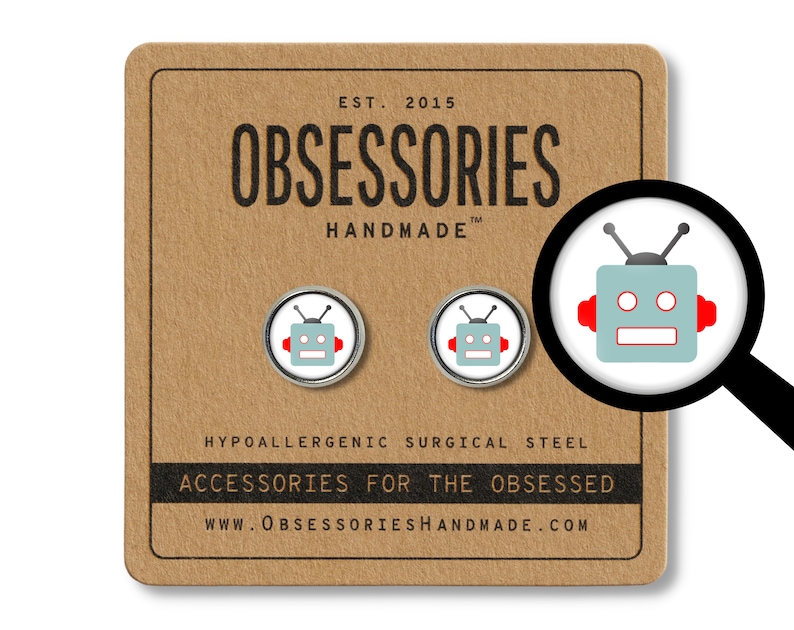 May include: A pair of silver robot earrings with red accents. The earrings are on a brown card with the text "OBSESSORIES HANDMADE" and "ACCESSORIES FOR THE OBSESSED".